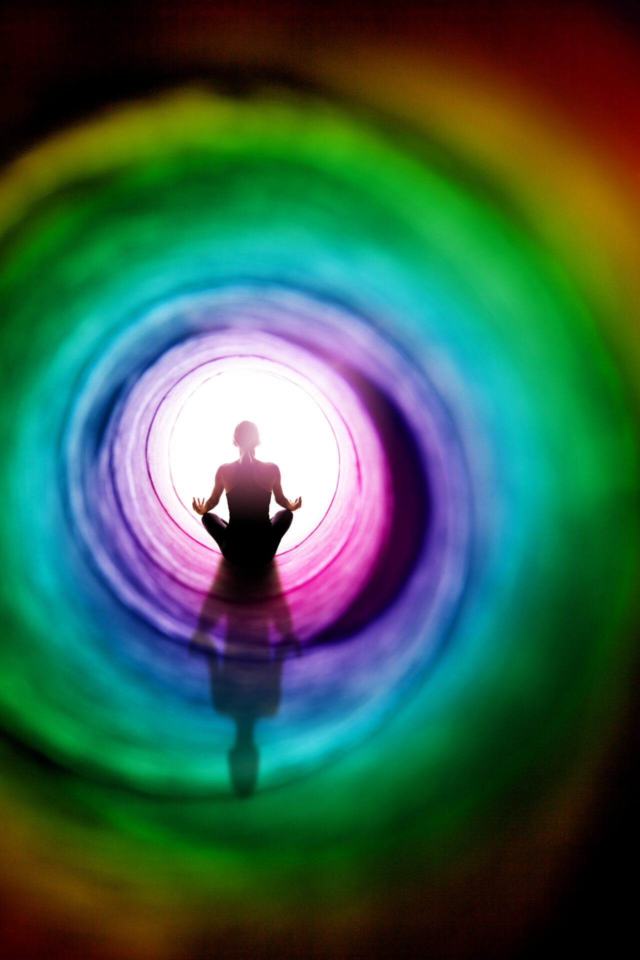 A conceptual image of the figure of a woman meditating by a colorful tunnel of light.