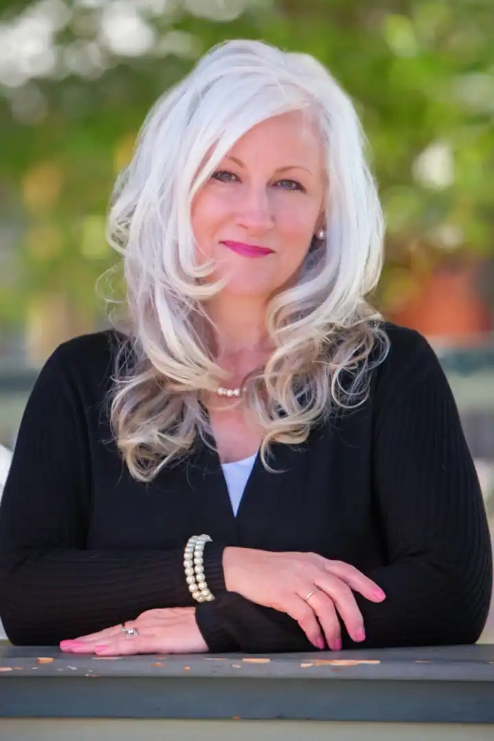 A woman with white hair and wearing pearls.